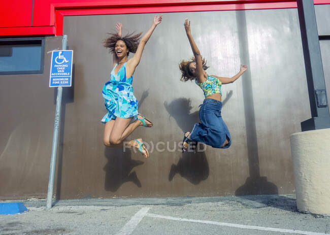Возбужденные подруги, прыгающие от радости к коричневой стене на парковке — стоковое фото