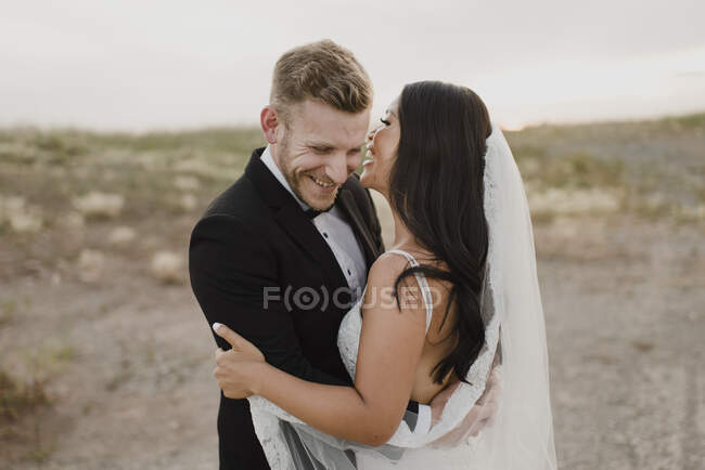 Joyeux marié embrassant mariée tout en se tenant dans le champ contre le ciel — Photo de stock