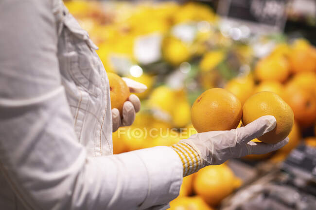 Hands with protectice gloves holding oranges, close-up — Stock Photo