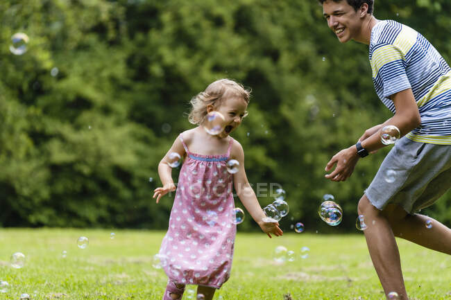 Cheerful brother playing with sister amidst bubbles at public park — Stock Photo
