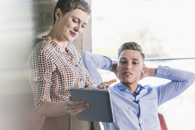 Businesswoman showing digital tablet to male coworker while discussing with him in office — Stock Photo