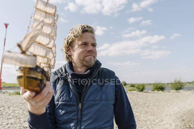 Maturo uomo tenendo giocattolo barca mentre in piedi vicino riva del fiume — Foto stock