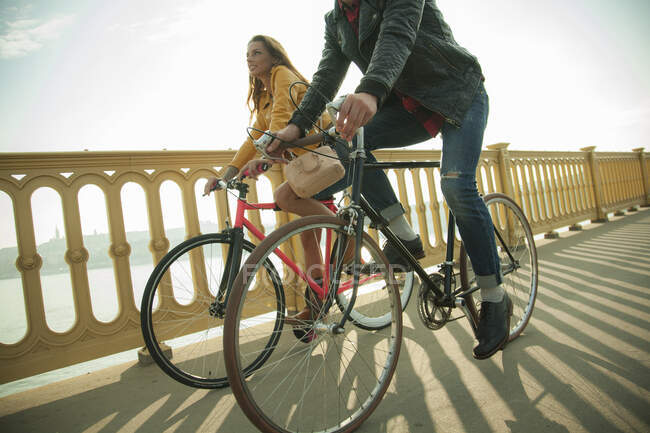 Couple hétérosexuel à vélo sur le pont contre le ciel — Photo de stock