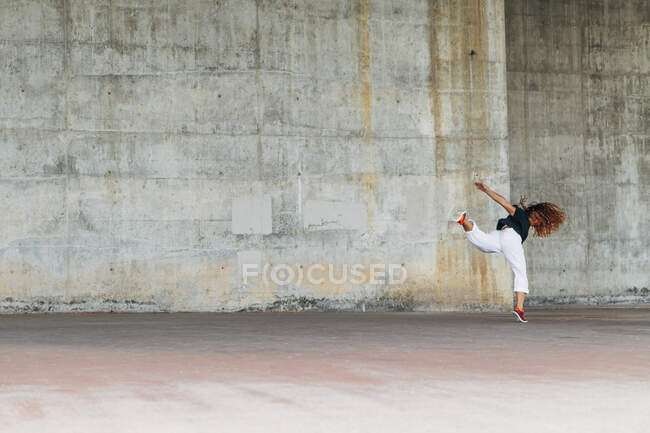 Молодая женщина делает акробатический прыжок во время тренировки против стены — стоковое фото
