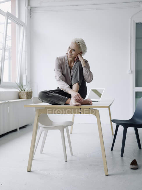 Улыбающаяся деловая женщина, размышляющая, сидя за столом в офисе — стоковое фото