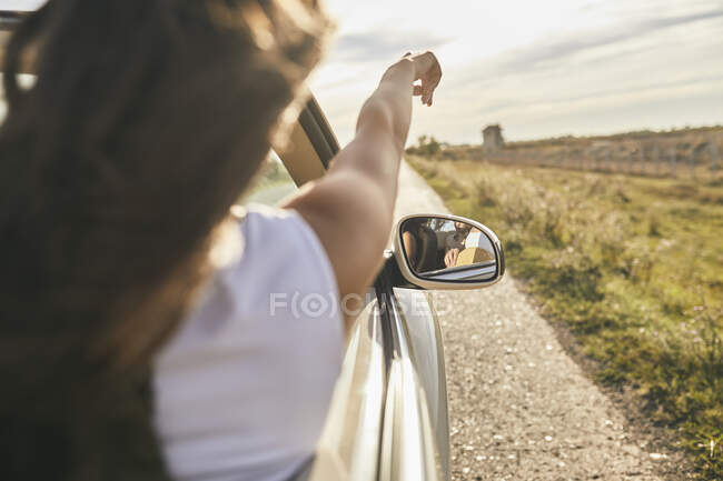 Молодая женщина, сидя в машине, указывает на облачное небо — стоковое фото