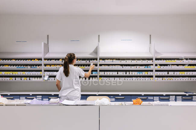Farmacéutica femenina que organiza los medicamentos en los estantes del hospital - foto de stock