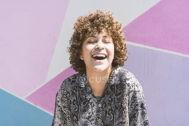 Весела жінка з закритими очима сидить на багатокольоровій стіні — стокове фото