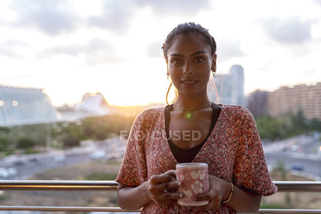 Mulher bonita segurando xícara de café enquanto está na varanda contra o céu — Fotografia de Stock