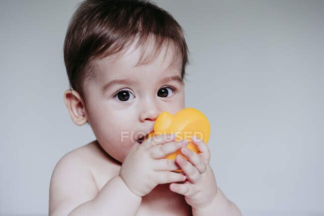 Милый маленький мальчик кладет игрушку себе в рот, сидя дома — стоковое фото