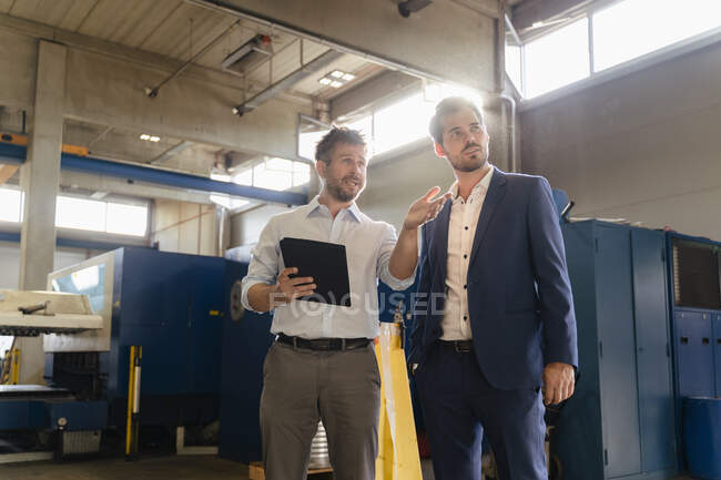 Kollege benutzt digitales Tablet, während er mit Geschäftsmann in der Fabrik diskutiert — Stockfoto
