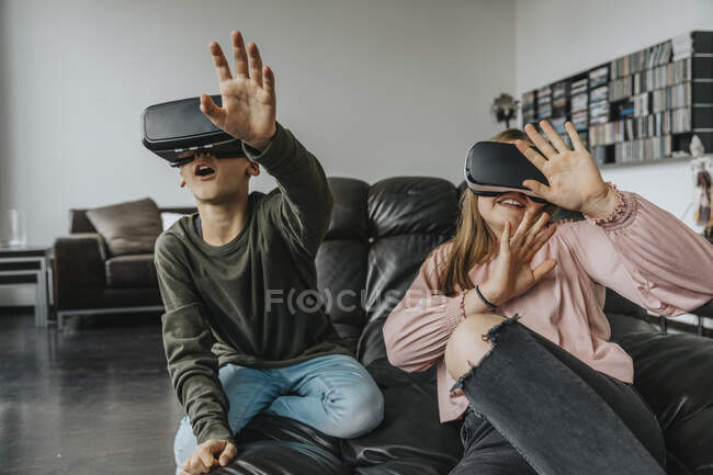 Amici allegri che guardano attraverso simulatori di realtà virtuale seduti sul divano a casa — Foto stock