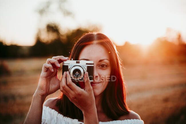 Mulher usando câmera vintage ao pôr do sol — Fotografia de Stock