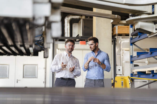 Des hommes d'affaires discutent pendant qu'ils se tiennent près d'un équipement en usine — Photo de stock