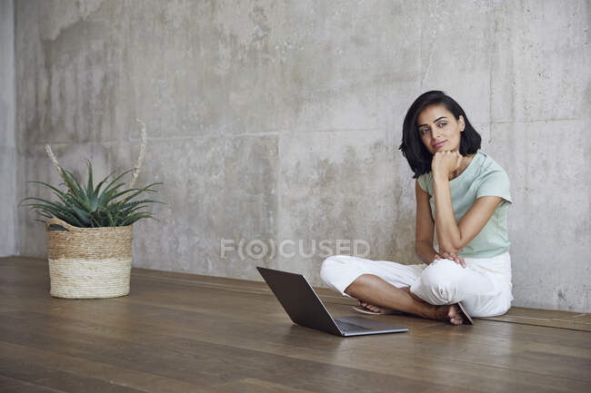 Imprenditrice donna premurosa seduta con computer portatile sul pavimento in legno massello contro parete in ufficio — Foto stock
