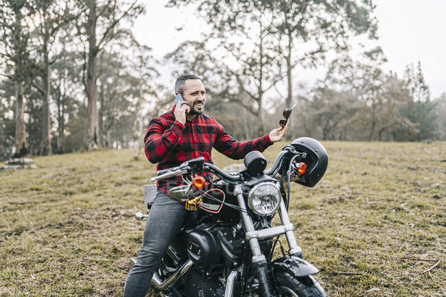 Hombre motociclista hablando por teléfono inteligente mientras está sentado  en motocicleta en el bosque — Caucásica, aventura - Stock Photo | #479975438