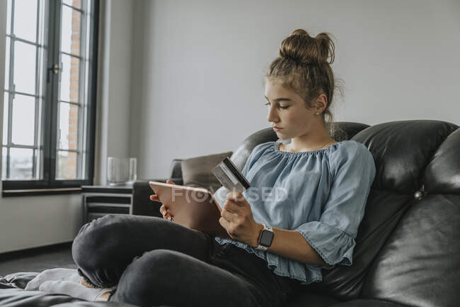 Girl with credit card doing online shopping over digital tablet while sitting on sofa at home — Stock Photo