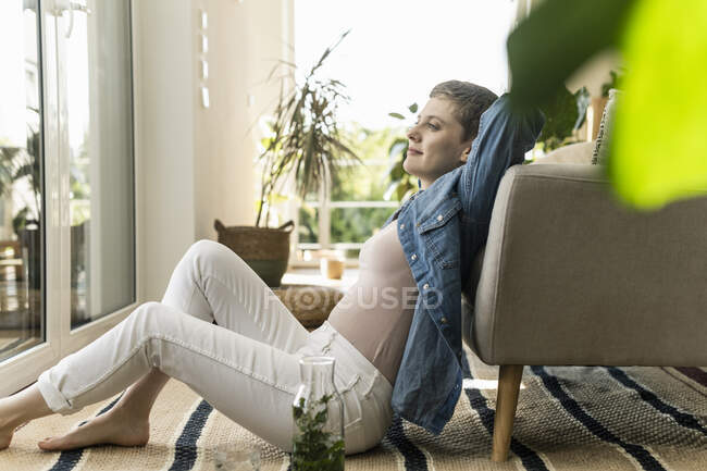Nachdenkliche erwachsene Frau sitzt zu Hause auf Teppich neben Sessel — Stockfoto