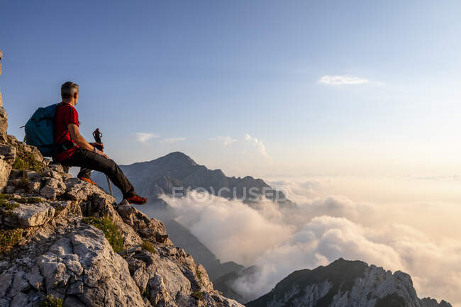 Excursionista admirando la vista mientras está sentado en la cima del pico de la montaña en los Alpes bergamascos, Italia - foto de stock