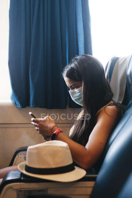 Mitte erwachsene Frau trägt Maske mit Handy, während sie auf Sitz im Kreuzfahrtschiff sitzt — Stockfoto