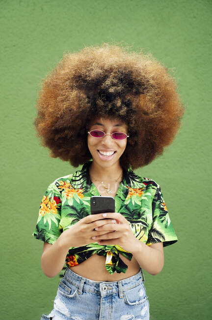 Giovane donna sorridente utilizzando smartphone davanti al muro verde — Foto stock