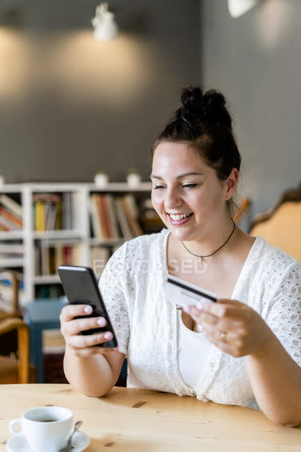 Sorrindo mulher voluptuosa fazendo compras on-line sobre o telefone móvel no café — Fotografia de Stock