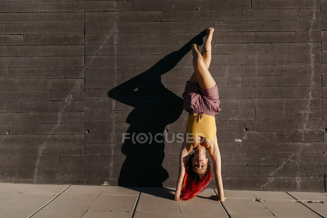 Jovem com cabelo vermelho realizando suporte contra a parede preta — Fotografia de Stock