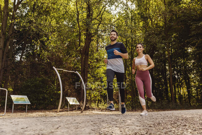 Homme et femme sportifs qui courent près d'un sentier de fitness — Photo de stock