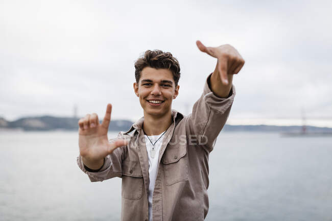 Joven sonriente mostrando señales de mano contra el cielo - foto de stock
