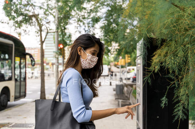 Mujer con máscara facial comprando billete de autobús durante COVID-19 - foto de stock