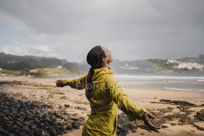 Mujer sonriente en impermeable en la playa durante la temporada de lluvias - foto de stock