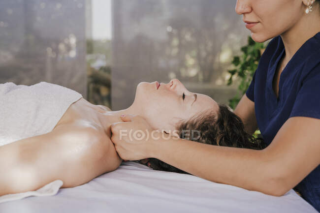 Gros plan d'une thérapeute massant le cou d'une cliente sur la table d'un spa de santé — Photo de stock