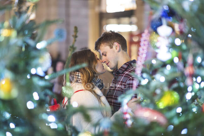 Young couple romancing while standing by illuminated Christmas tree at night — Photo de stock