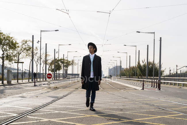 Ragazzo alla moda che cammina tra binario ferroviario su strada — Foto stock