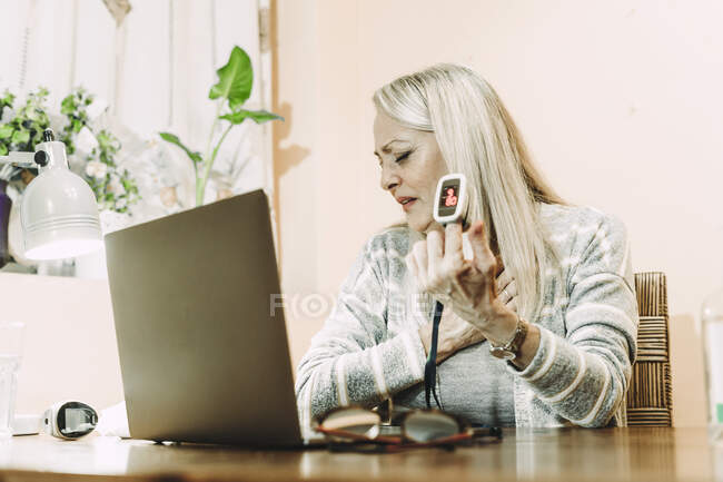 Femme âgée dans la peur montrant oxymètre de pouls sur ordinateur portable lors de la consultation en ligne à la maison — Photo de stock