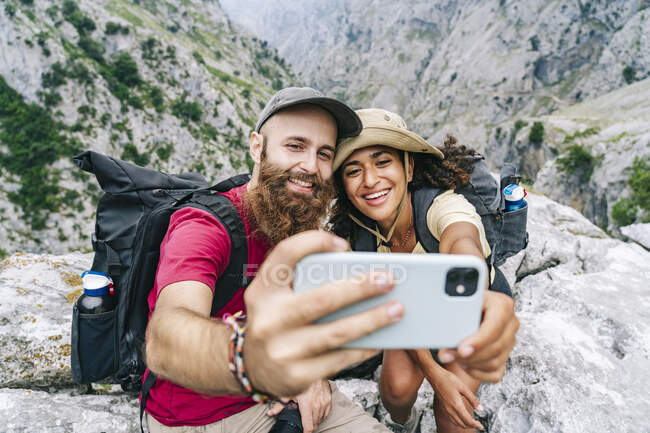 Coppia sorridente mentre prende selfie seduto sulla cima della montagna a Ruta Del Cares, Asturie, Spagna — Foto stock