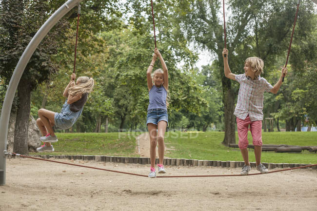 Happy boy and girls hanging on rope at playground in park — Stock Photo