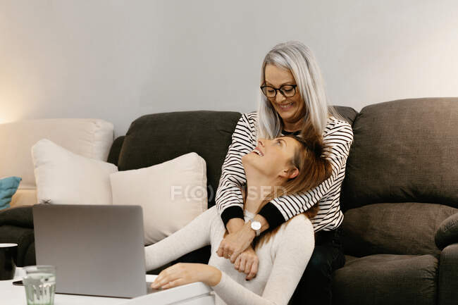 Feliz madre con el brazo alrededor de la hija sentada en casa - foto de stock