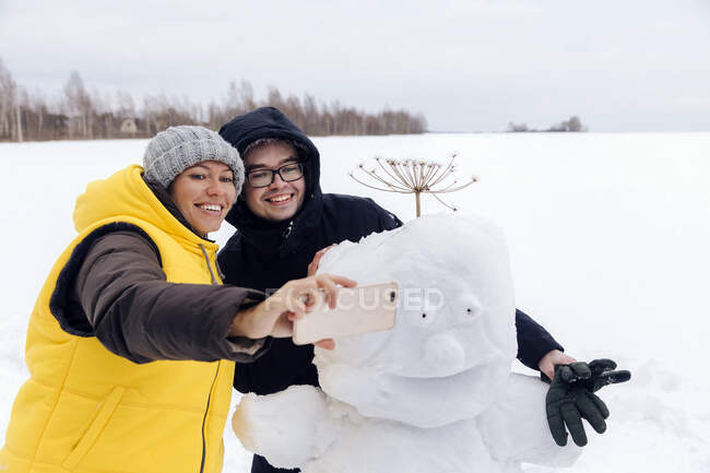 Smiling couple taking selfie with snowman — Stock Photo