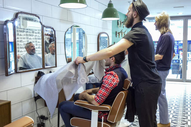 Homme salon de coiffure tenant tablier devant le client au salon de coiffure — Photo de stock