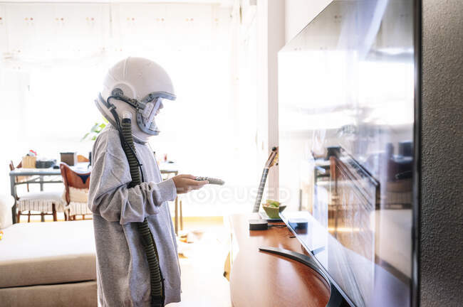 Garçon portant un casque spatial regarder la télévision tout en étant debout à la maison — Photo de stock