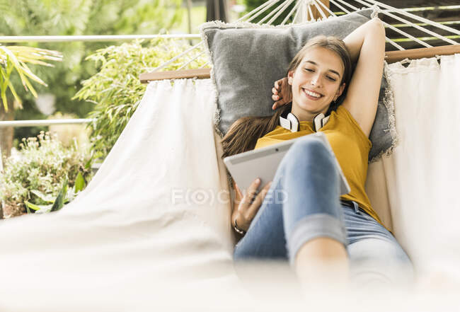 Усмішка красивої жінки за допомогою цифрового планшета, розслабляючись на гамаку на подвір'ї — стокове фото