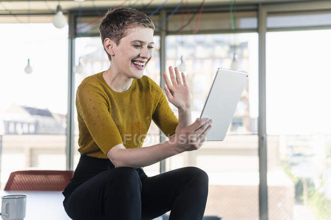 Happy businesswoman sitting on desk in office having a video conference — Foto stock