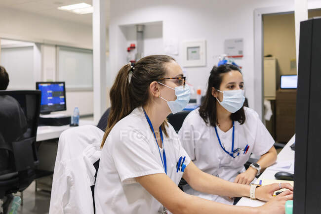 Le farmaciste che indossano maschere discutono al computer mentre sono sedute in ospedale — Foto stock