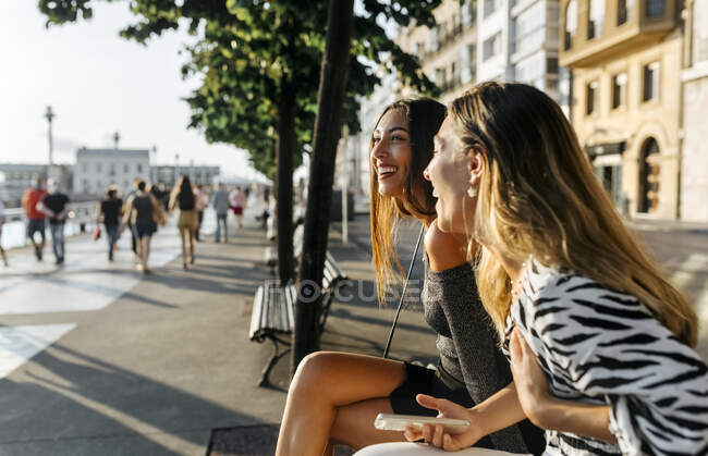 Des amis heureux souriant assis à la promenade pendant le coucher du soleil — Photo de stock