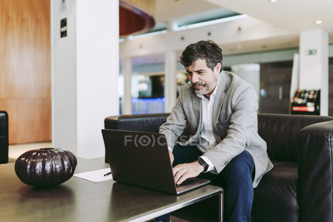 Empreendedor masculino usando laptop enquanto sentado no lobby do hotel — Fotografia de Stock