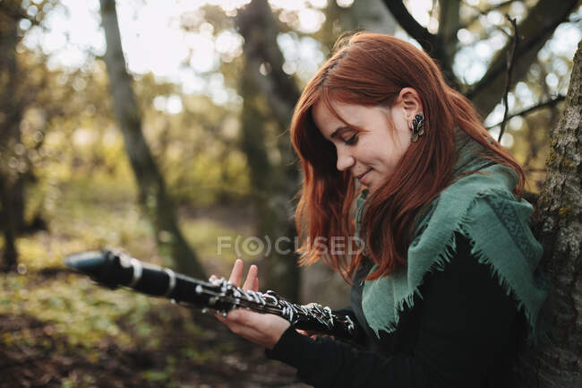 Femme musicienne rousse regardant un instrument en forêt pendant l'automne — Photo de stock