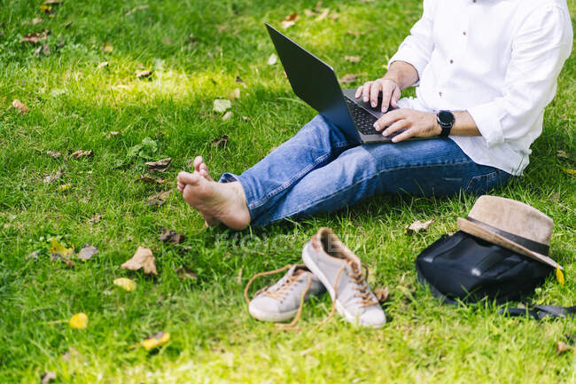 Mature homme en utilisant un ordinateur portable tout en étant assis dans le parc public — Photo de stock