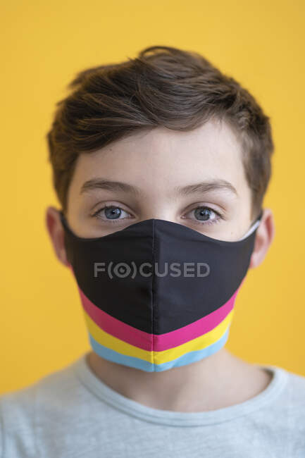 Gros plan d'un garçon portant un masque multicolore sur fond jaune — Photo de stock