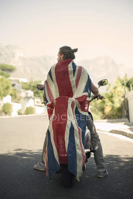 Uomo avvolto nella bandiera nazionale seduto sulla moto durante l'estate — Foto stock